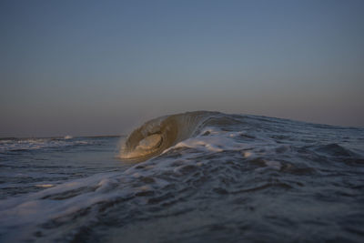 Waves splashing in sea against clear sky during sunset