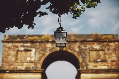 Low angle view of lighting equipment hanging on tree against built structure