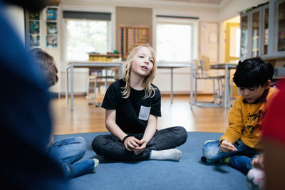 Girl talking while sitting with friends on floor in classroom