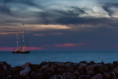 Sailboat on sea against cloudy sky during sunset