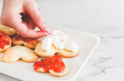 Hands of a girl laying coffee cups heart sprinkles on not perfect freshly baked heart cookies 