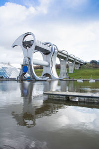 Reflection of metal structure in lake against sky