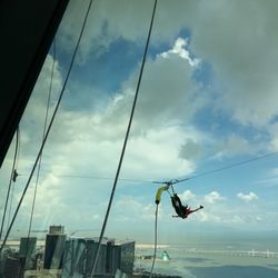 Low angle view of people hanging on rope against sky