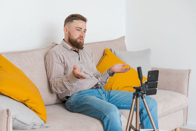 Smiling bearded guy filming video using smartphone on tripod online while