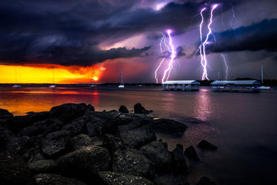 Lightning over sea against dramatic sky during sunset