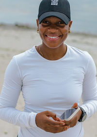 Portrait of young woman standing at beach holding a smartphone