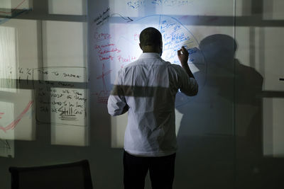 Rear view of businessman writing on whiteboard over tablet computer in office