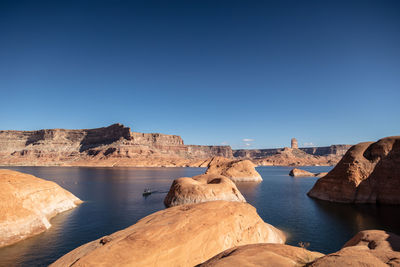 Rock formations by sea against clear blue sky