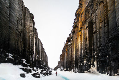 Unrecognizable traveler walking in between spectacular scenery of rocky ravine with frozen river in highlands in iceland