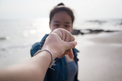 Cropped image of woman holding friend hand at beach against sky