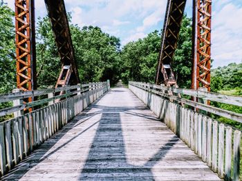 Bridge leading towards trees during sunny day