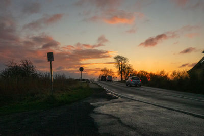 Road by trees against sky during sunset