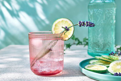 Lavender lemonade with lime slices and lavender flower in pink glass near pastel light blue surface. 