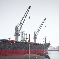 Cranes at commercial dock against clear sky