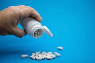 Close-up of hand holding bottle against blue background