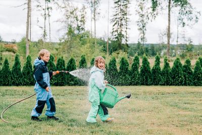 Brother and sister playing in the rain with a hose and watering can