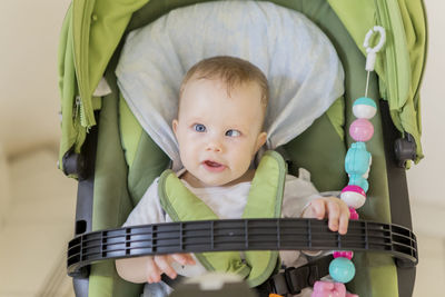 Cute baby girl sitting in carriage at home