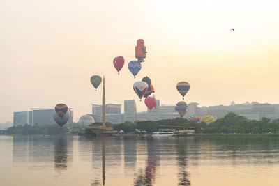 Hot air balloon flying over river against sky during sunset