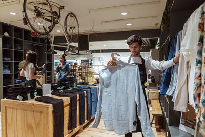 Salesman arranging clothes on rack while saleswoman assisting customers at store