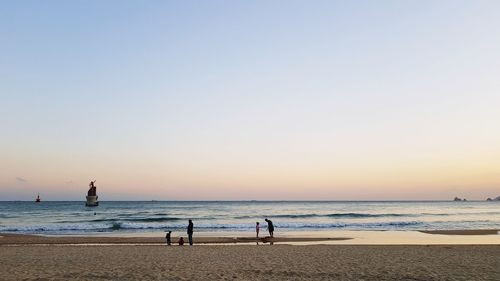 People at beach against clear sky during sunset