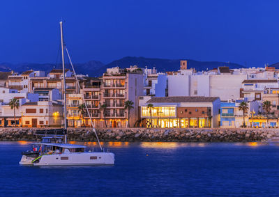 Sailboats in sea by buildings against blue sky