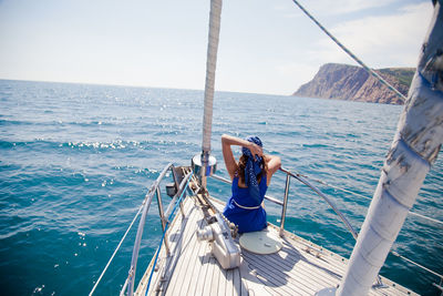 Young woman on nose of the white yacht in a nautical theme. blue jacket, blue scarf and sunglasses.