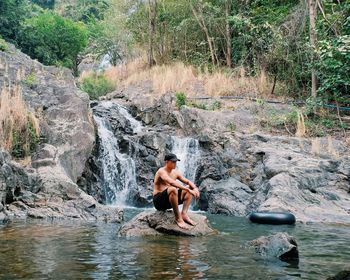 Full length of shirtless man sitting on rock