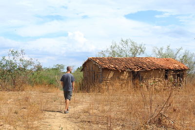 Rear view of man walking on field against sky