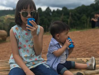 Siblings playing with toy mobile phone against trees