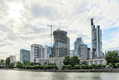 Modern cityscape by river against sky