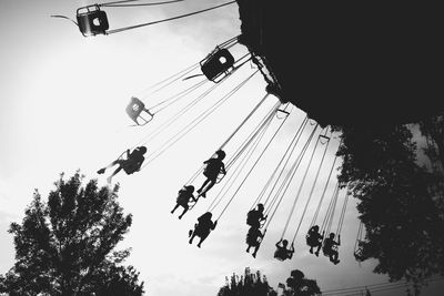 Low angle view of silhouette people enjoying chain swing ride against sky