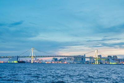 Suspension bridge over sea against cloudy sky