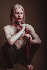 Shirtless man sitting against brown background