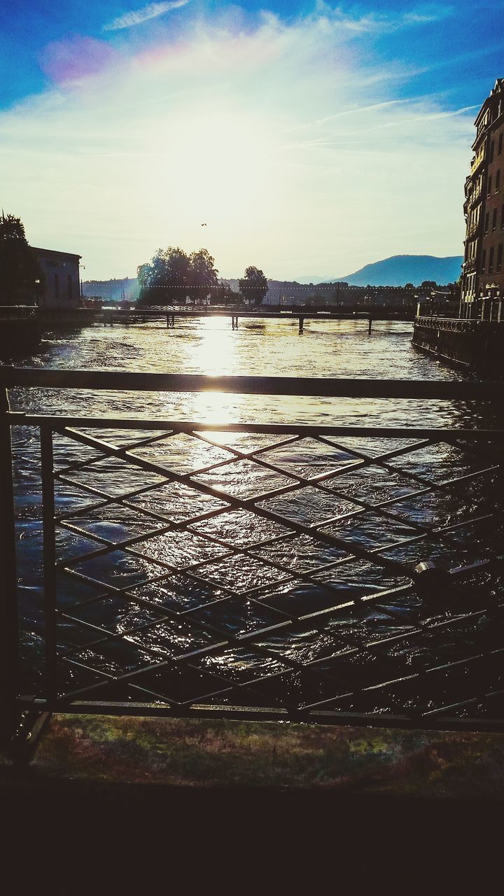 water, sky, architecture, built structure, building exterior, sunset, river, cloud - sky, city, sunlight, cloud, reflection, sea, railing, outdoors, nature, sun, no people, silhouette, tree