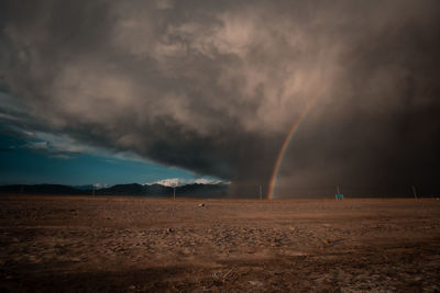 Scenic view of rainbow over land against cloudy sky