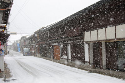 Snow covered road by buildings against sky in city