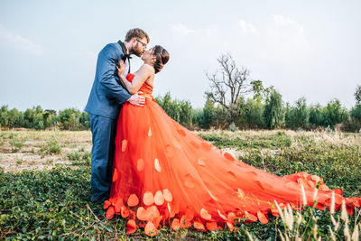 Side view of newlywed couple kissing on field against sky