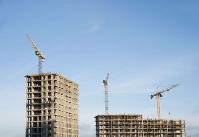 Low angle view of crane by building against sky