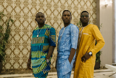 Men in traditional clothing looking away while standing with hands in pockets at banquet