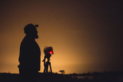 Side view of silhouette man standing by camera tripod during sunset