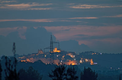 View of ostuni. silhouette trees and illuminated mountains against village, sky at sunset