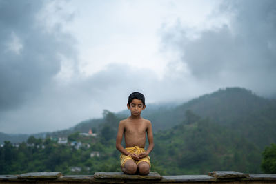 A young indian cute kid doing yoga in the mountains,wearing a dhoti