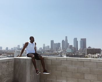 Man sitting on terrace in city against clear blue sky