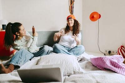 Young woman photographing female friend through smart phone at home