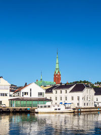 Buildings by river against clear blue sky