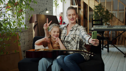 Smiling mother and daughter taking selfie at home