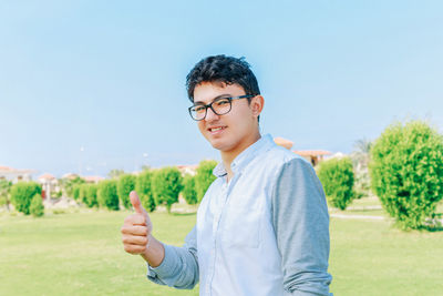 Portrait of man showing thumbs up sign while standing on field against sky