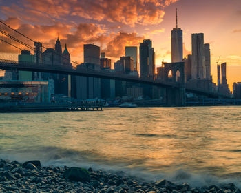 Modern buildings by sea against sky during sunset