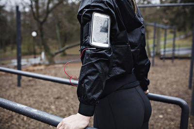 Rear view midsection of female athlete wearing arm band while exercising on parallel bars in forest