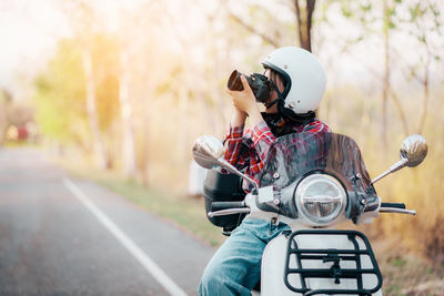 Rear view of man riding motor scooter on road